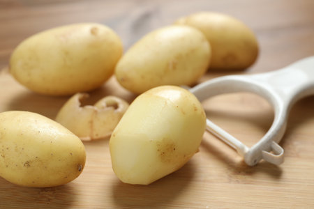 Fresh raw potatoes and peeler on wooden table, closeupの写真素材