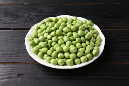 Fresh green peas in bowl on black wooden tableの写真素材