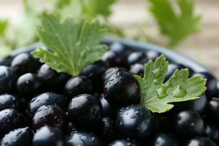 Ripe blackcurrants in bowl and green leaves on wooden table, closeupの写真素材