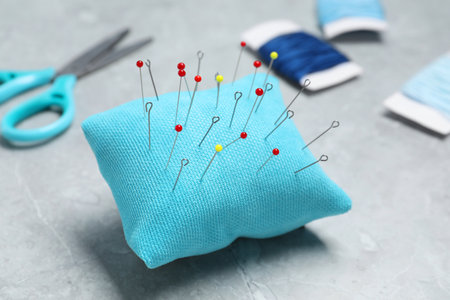 Light blue pincushion with sewing pins on gray table, closeup