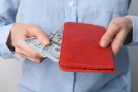 Woman putting dollar banknotes into wallet on light background, closeup