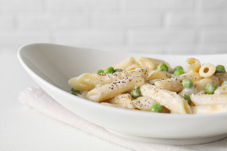Delicious pasta with green peas and creamy sauce in bowl on white table, closeupの写真素材