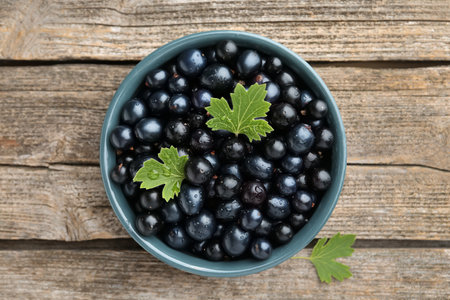 Ripe blackcurrants in bowl and green leaves on wooden table, top viewの写真素材