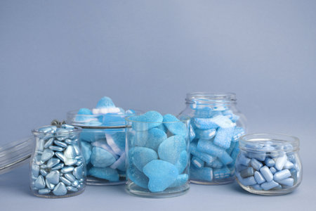 Many bright candies in glass jars on light blue background. Space for textの写真素材