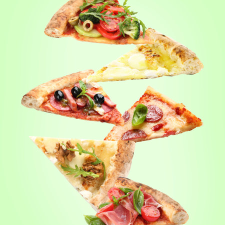 Slices of different pizzas in air on light green backgroundの写真素材