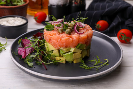Tasty salmon tartare with avocado and greens on white wooden table, closeupの写真素材