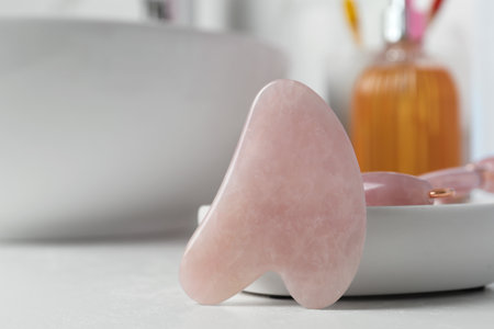 Rose quartz gua sha tool and natural face roller on white table, closeupの写真素材