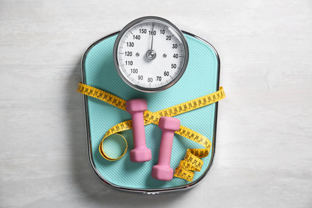 Bathroom scale, measuring tape and dumbbells on white wooden background, flat layの写真素材