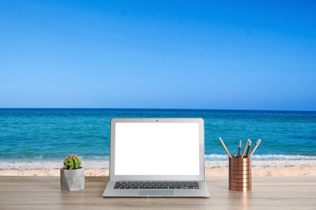 Workplace at beach, distant office. Table with laptop on sandy seashore. Mockup for designの写真素材
