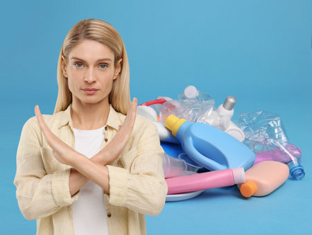 Environmental pollution. Woman showing stop gesture, heap of garbage on light blue backgroundの写真素材