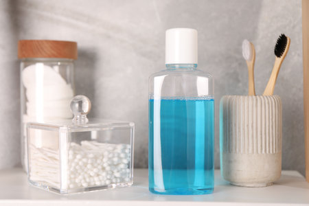 Bottle of mouthwash, toothbrushes, cotton buds and pads on white shelf in bathroomの写真素材