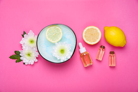 Flat lay composition with bowl of water, flowers and lemons on pink background. Spa treatment