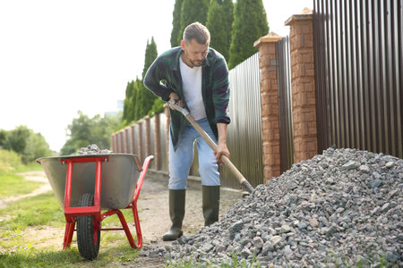 Man picking stones up with shovel and wheelbarrow outdoorsの写真素材