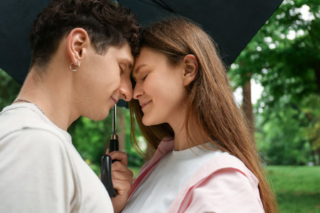 International dating. Lovely young couple with umbrella spending time together in parkの写真素材
