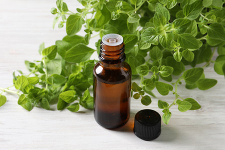 Essential oil in bottle and oregano leaves on white wooden table, closeupの写真素材
