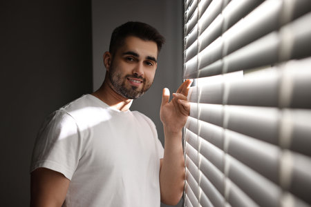 Man near window blinds at home, space for textの写真素材