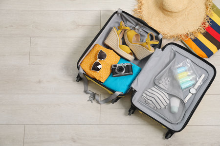 Open suitcase with traveler's belongings on floor, flat lay. Space for text