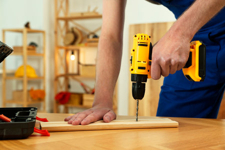 Craftsman working with drill at wooden table in workshop, closeupの写真素材
