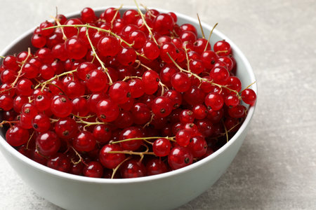 Fresh red currents in bowl on light gray table, closeup