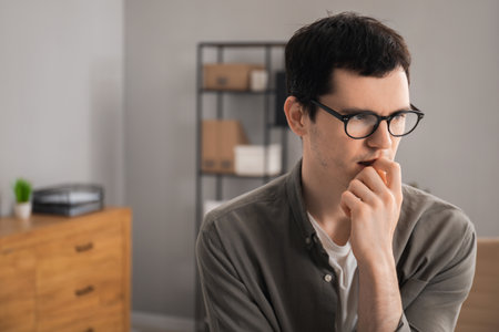 Embarrassed young man in glasses in office, space for textの写真素材