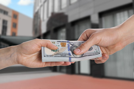Client giving money to real estate agent against building, closeup