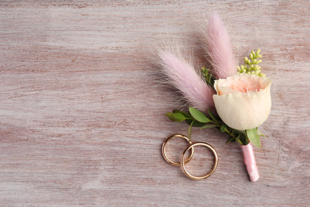 Small stylish boutonniere and rings on light wooden table, top view. Space for textの写真素材