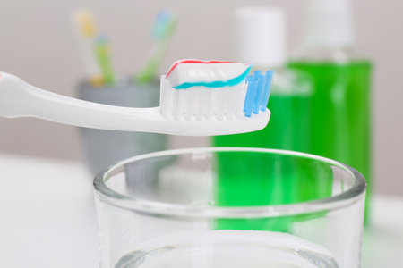 Toothbrush with paste near mouthwash on blurred background, closeup