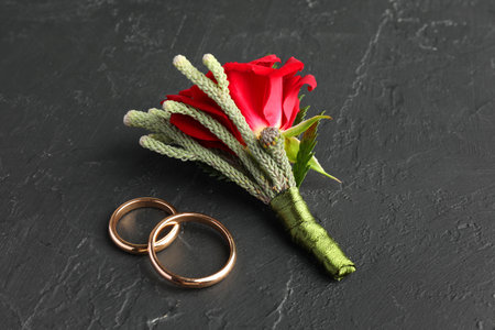 Stylish red boutonniere and rings on black table