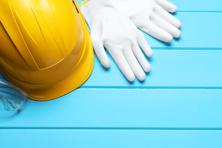 Hard hat, protective gloves and goggles on light blue wooden background, flat lay. Space for textの写真素材
