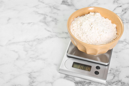 Kitchen scale with bowl of flour on white marble table, closeup. Space for textの写真素材