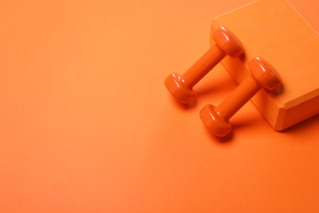 Dumbbells and yoga block on orange background. Space for textの写真素材