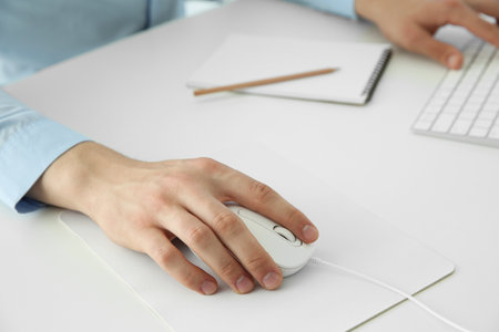 Man working with wired mouse and computer keyboard at white table indoors, closeupの写真素材