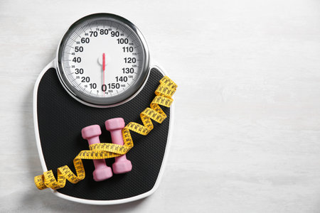 Scale, dumbbells and measuring tape on white wooden background, top view. Space for textの写真素材