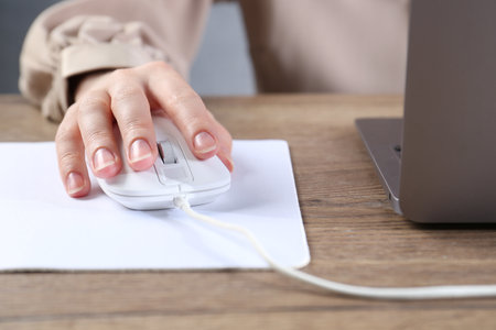 Woman using computer mouse while working with laptop at wooden table, closeupの写真素材