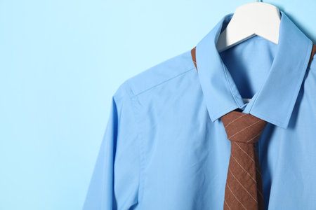 Hanger with shirt and brown necktie on light blue background, closeup. Space for textの写真素材