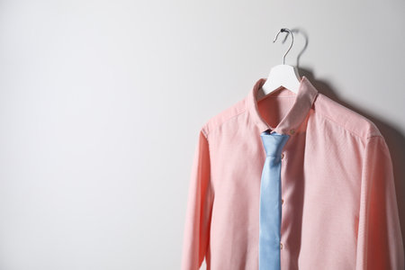 Hanger with shirt and necktie on light wall, space for textの写真素材