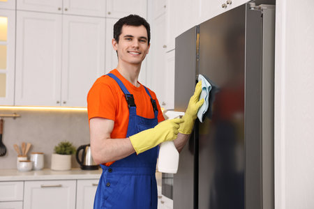 Professional janitor wearing uniform cleaning fridge in kitchenの写真素材