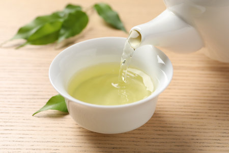 Pouring refreshing green tea into cup at wooden table, closeupの写真素材