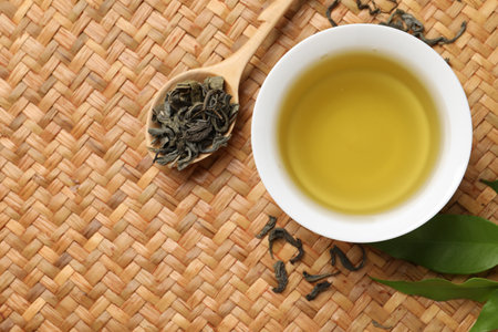 Refreshing green tea in cup, spoon and leaves on table, flat lay. Space for text