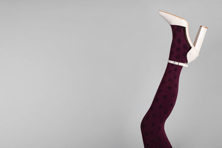 Woman wearing tights and high heel shoe on gray background, closeup. Space for text