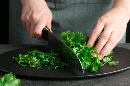 Woman cutting fresh coriander at gray textured table, closeup