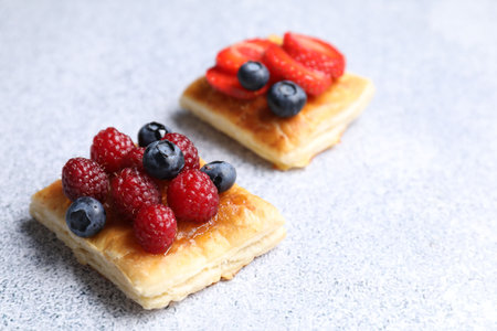 Tasty puff pastries with berries on light gray table, closeup. Space for textの写真素材