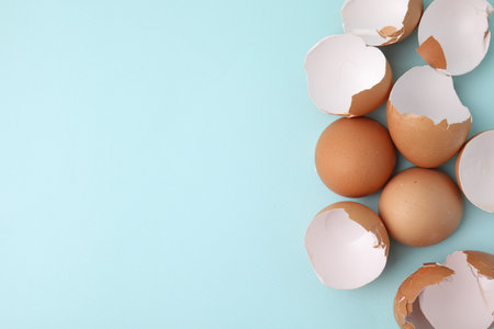 Broken eggshells on light blue background, top view. Space for text