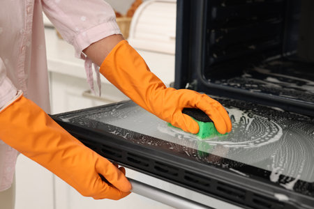 Woman cleaning oven door with sponge in kitchen, closeupの写真素材