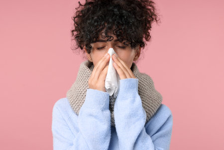 Cold symptom. Young woman with tissue on pink background