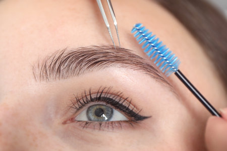 Beautician making eyebrow correction to young woman, closeupの写真素材