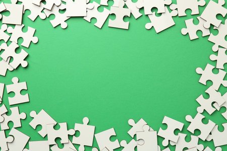 Frame of white puzzle pieces on green background, top view. Space for textの写真素材