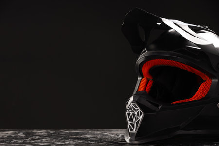 Modern motorcycle helmet with visor on grey stone surface against black background, closeup. Space...
