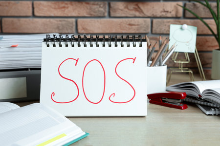 Notebook with word SOS and stationery on wooden table at workplaceの写真素材