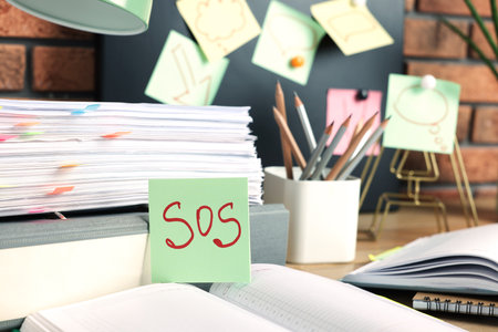 Sticky note with word SOS and stationery on table at workplaceの写真素材